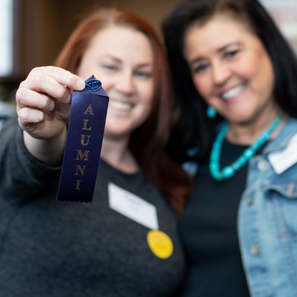 Two NAU alumni holding up pins that read, "Alumni."