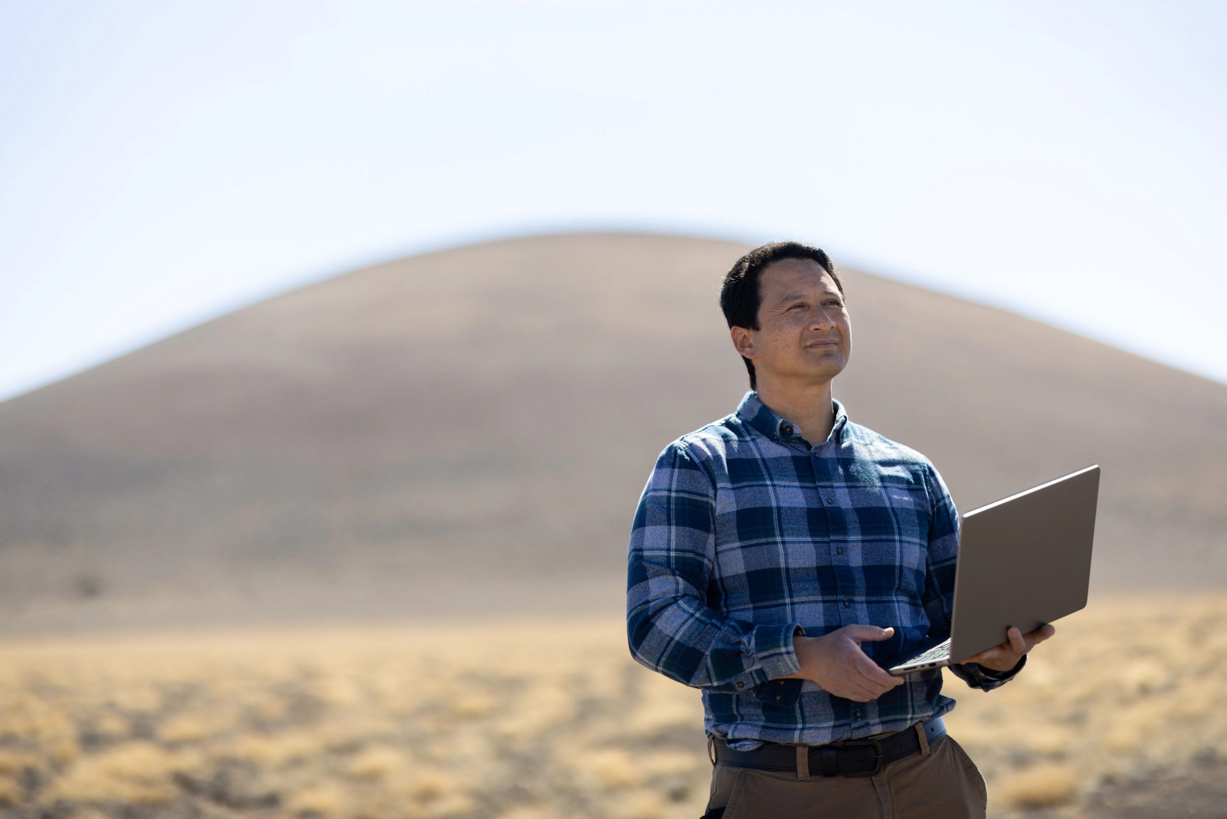 Frank Telles holding laptop computer while doing dust and drought research at study site.