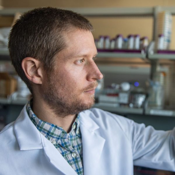 Jason Ladner, in his lab, looking at a vial that has liquid in it.