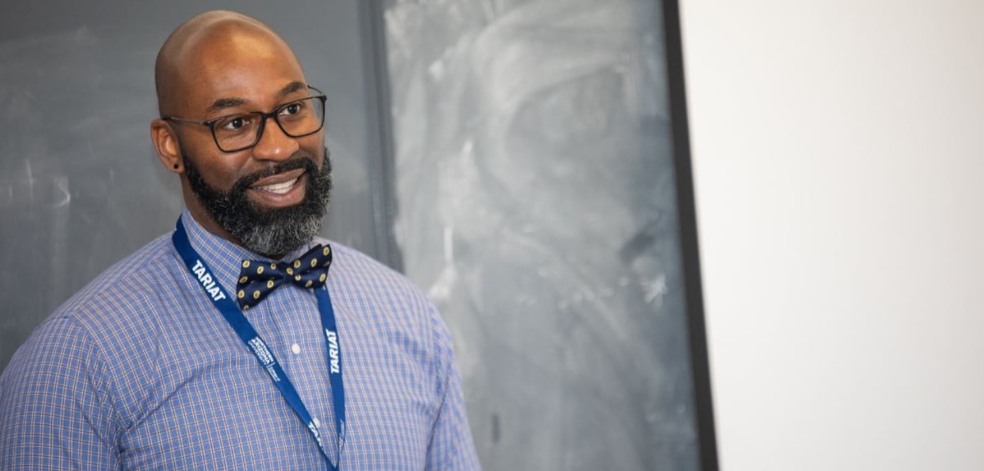 A man in a bow tie and an NAU lanyard stands at a chalkboard