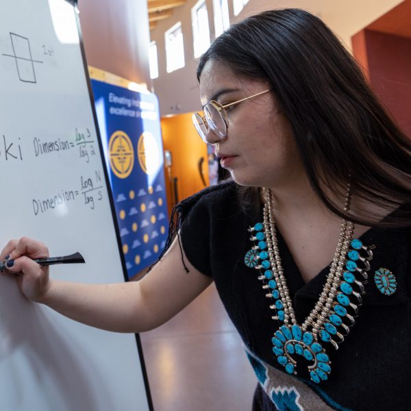 Kaylin McLiverty writes geometric terms with their weaving pattern names, along with drawings and equations on a white board.
