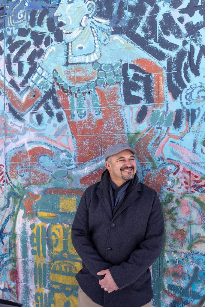 NAU alumnus and Coconino County Board of Supervisors vice chair Jeronimo Vasquez stands in front of mural that depicts Mesoamerican culture.