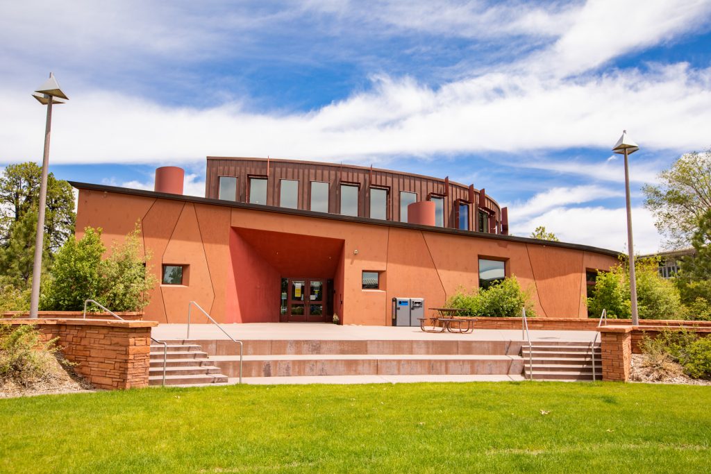 Native American Cultural Center in the summer with green grass, leafy trees and bushes, and wispy, white clouds.