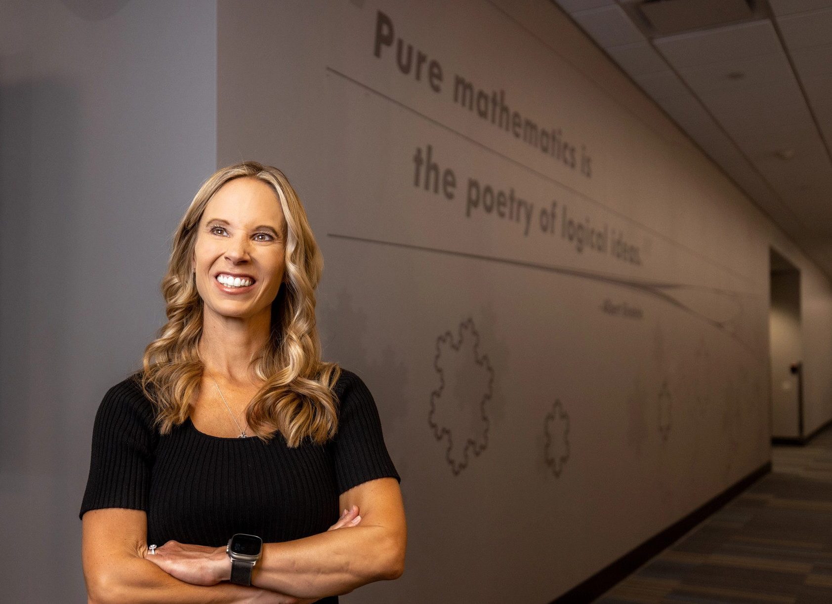 Mathematics Associate Professor Angie Hodge-Zickerman stands by wall in math lab that reads: "Pure mathematics is the poetry of logical ideas."