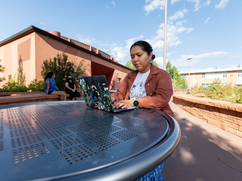 Student sitting outside the Center for Native American and Indigenous Futures (CNAIF) working on a computer.