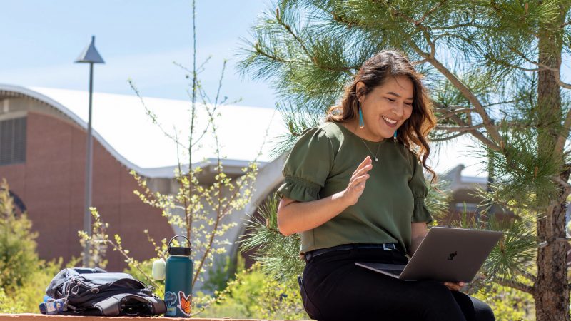 Student writing on laptop outside.