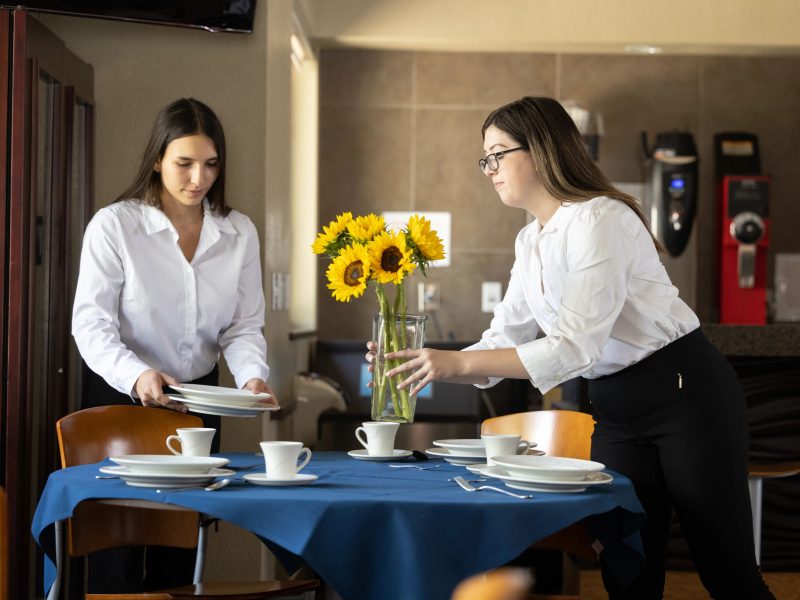 H R M students setting up a dining table with flowers and silverware.