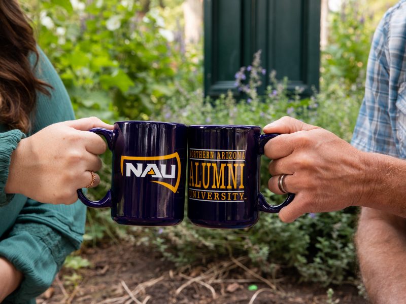Two N A U alumni clinking coffee cups together.