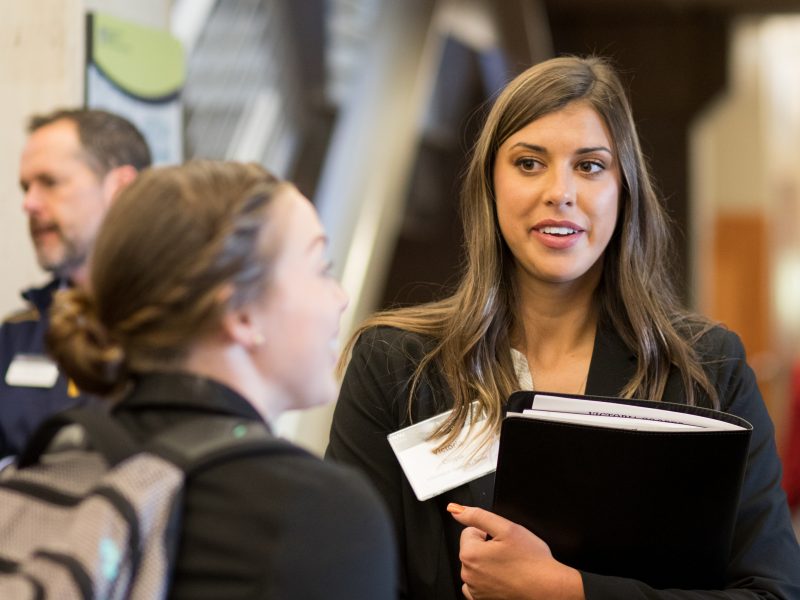 Professionally dressed business students chatting in the halls of the college of business carrying notebooks and supplies.