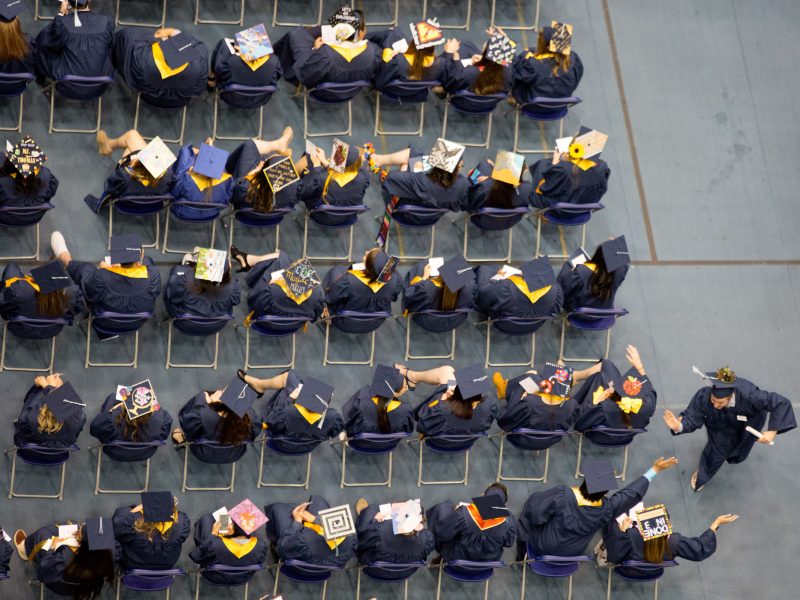 Overview of students in graduation regalia from above featuring two students exchanging a high-five.