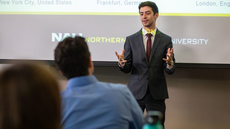 Student presenting in front of a projector screen that reads, 'Northern Arizona University'.