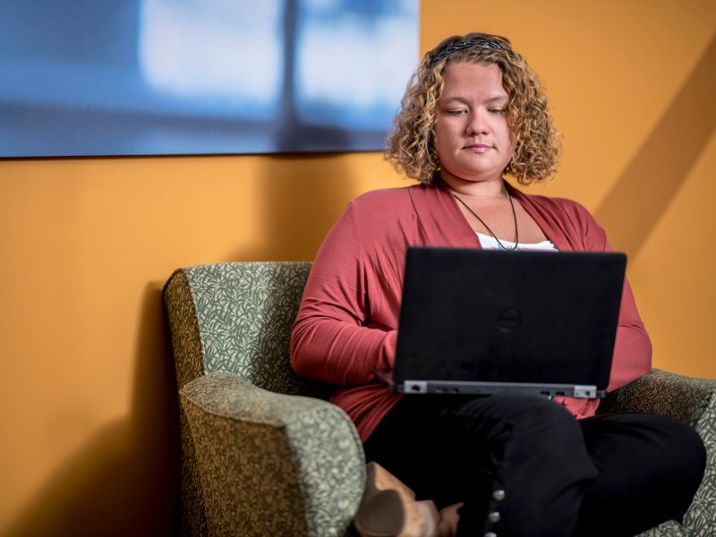 An N A U student sitting on a couch, looking at their laptop.
