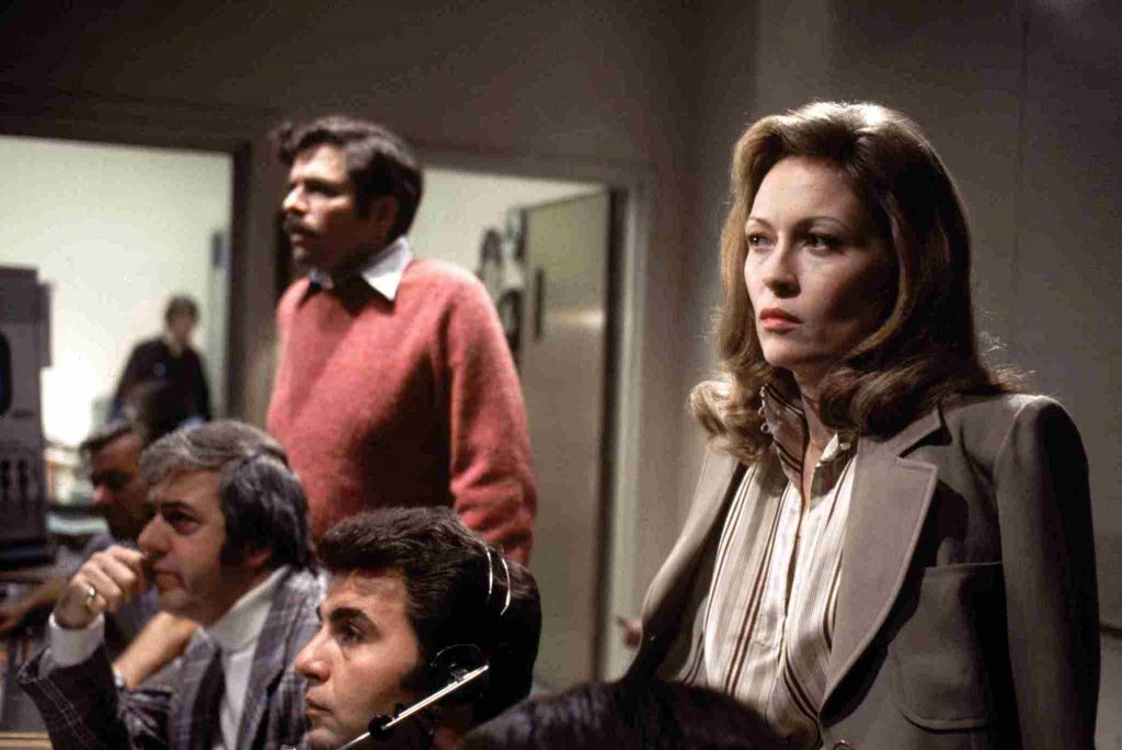 Scene from "Network "with Faye Dunaway - 1970's newsroom with four people watching from behind scenes looking serious