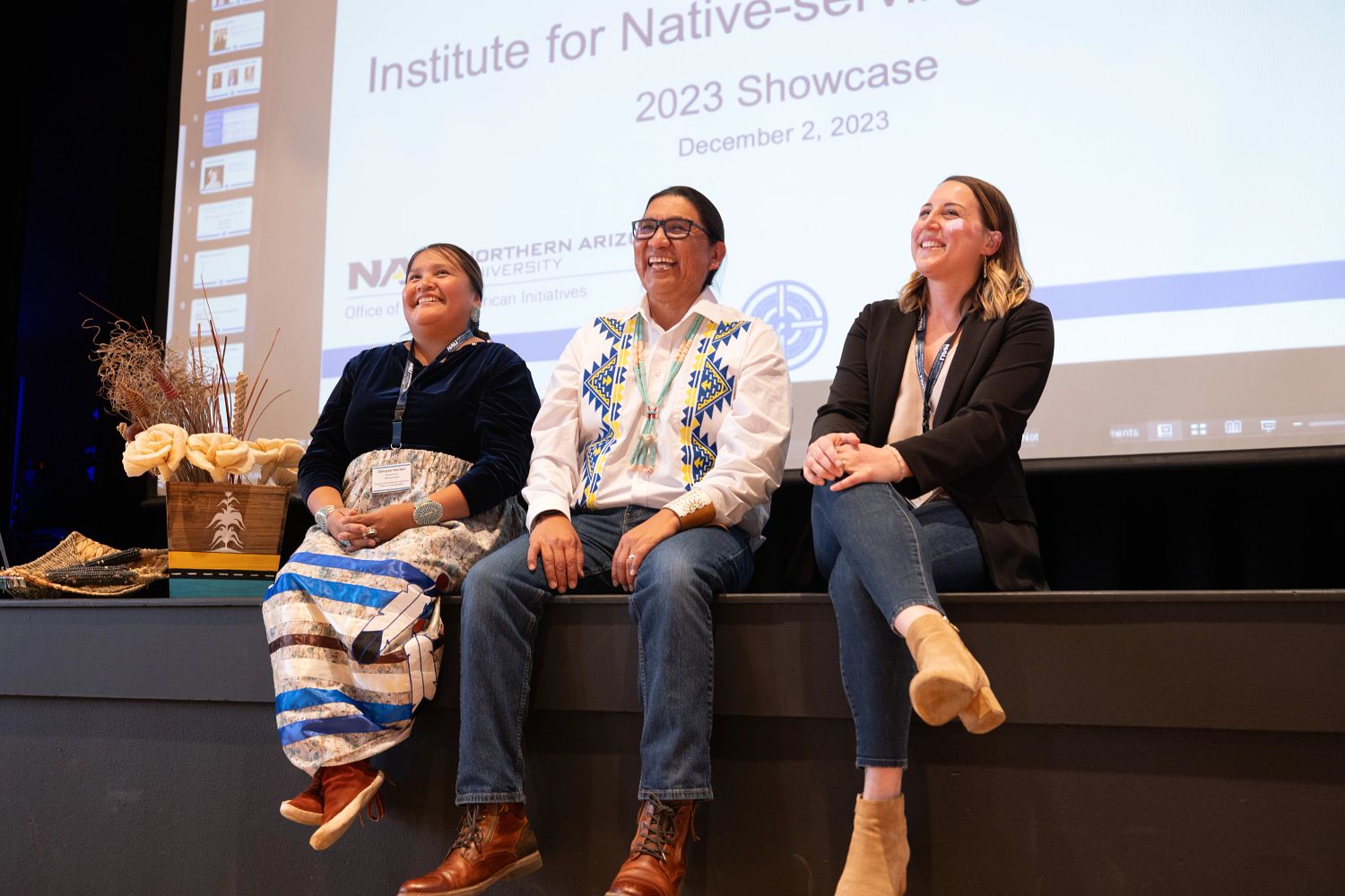 Three people sitting on the stage in front of a projector screen.