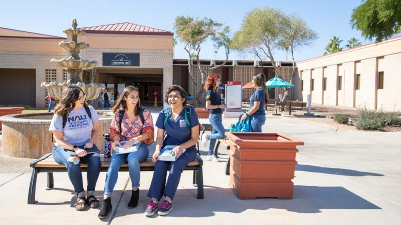 Tres estudiantes se sientan en una banca en frente de la fuente en el campus de NAU-Yuma.