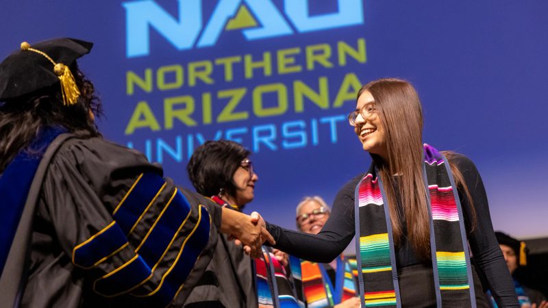 Un graduado de NAU acepta su diploma de un miembro de facultad en su ceremonia de graduación.