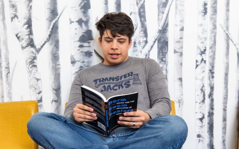 Estudiante de NAU sentado en una silla leyendo un libro.