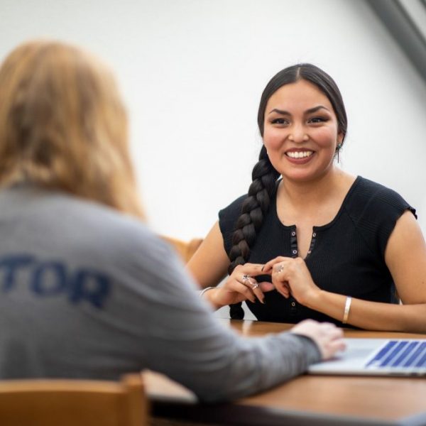 El estudiante de música Sage Bond se sienta en una mesa frente a un mentor estudiantil de NAU.