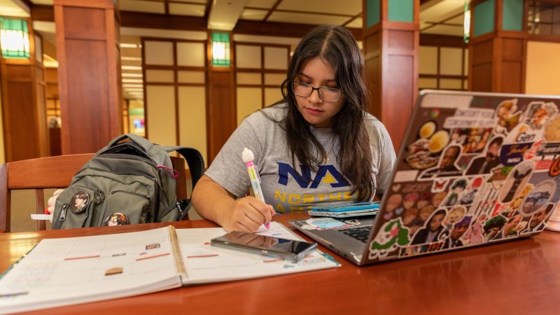 Un estudiante de NAU sentado enfrente de una computadora portátil en la biblioteca Cline tomando apuntes.