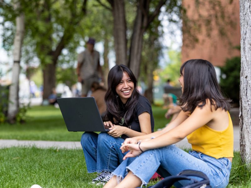 Dos estudiantes de NAU se sientan juntos en el North Quad bajo un árbol.