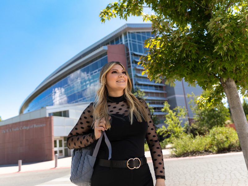 Estudiante de Mercadotecnia de NAU Ana Aranda camina a través de campus en un día soleado.