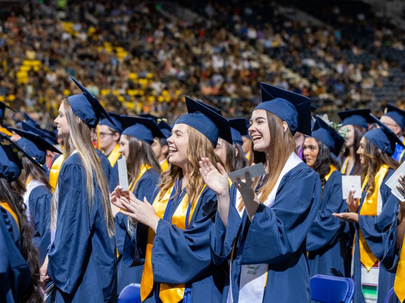 New graduate students standing and clapping during commencement.