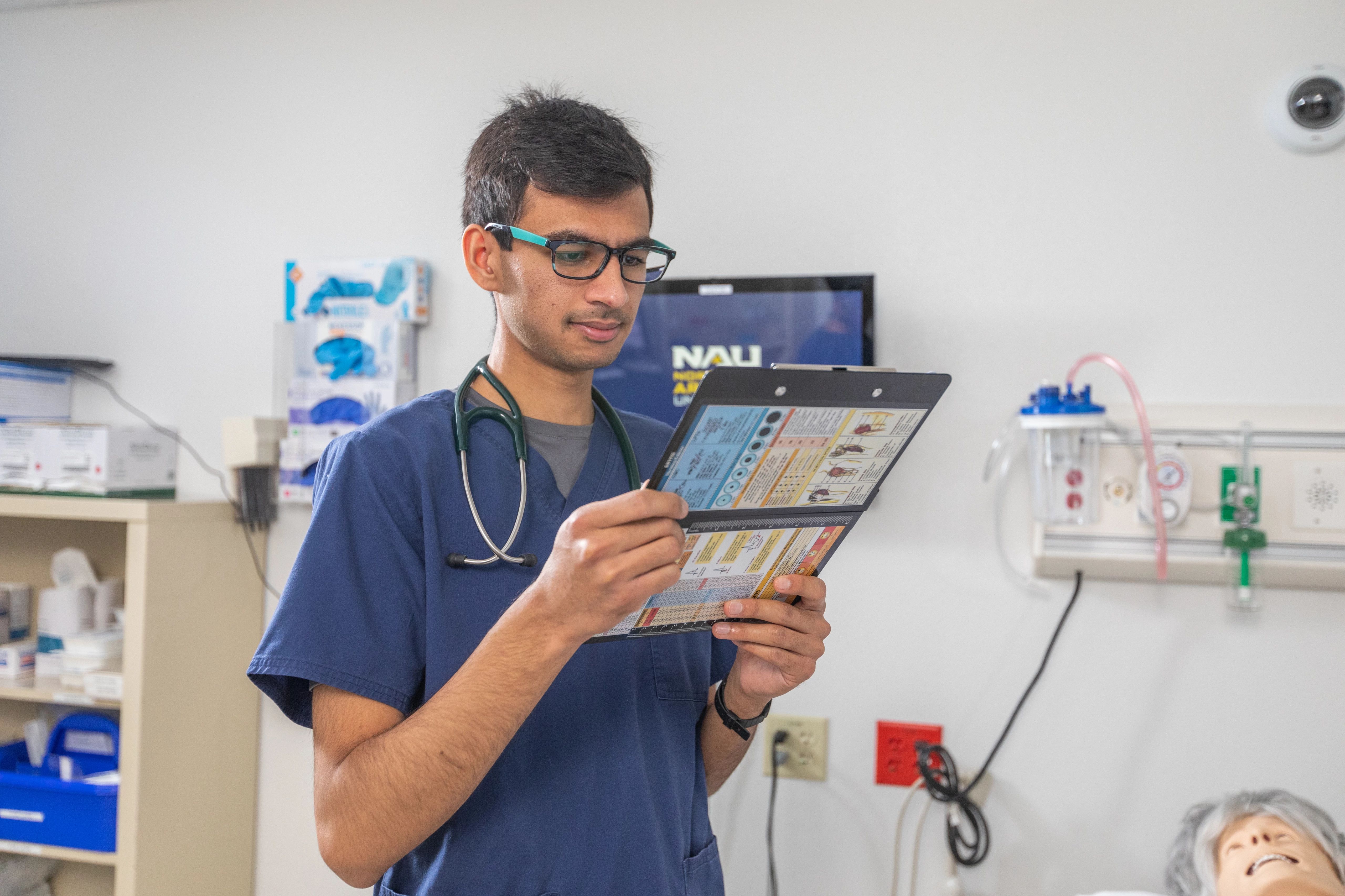 NAU nursing student dressed in scrubs looking at a patient chart