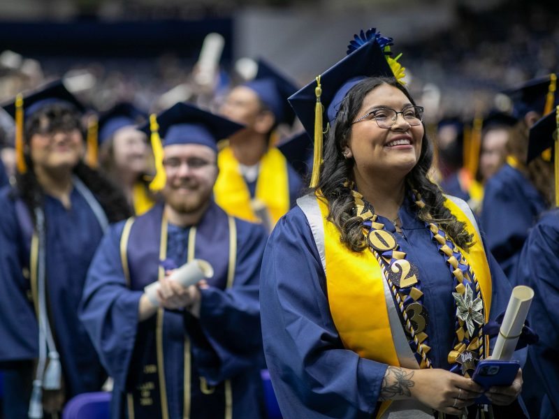 NAU grads standing, smiling, and holding their diplomas at the end of Commencement