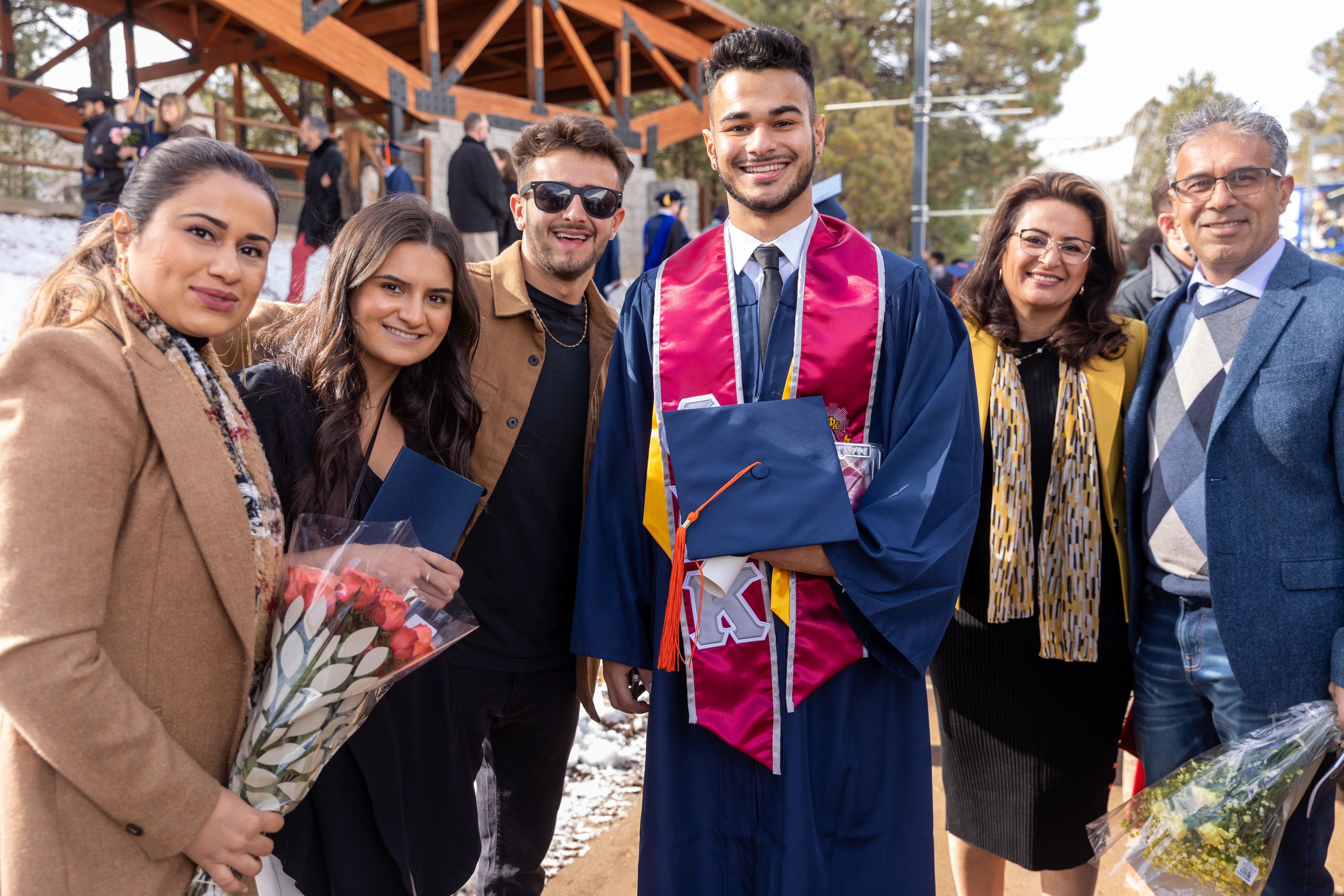Male NAU graduate wearing gown and stole, and holding his cap, poses for a photo with his family