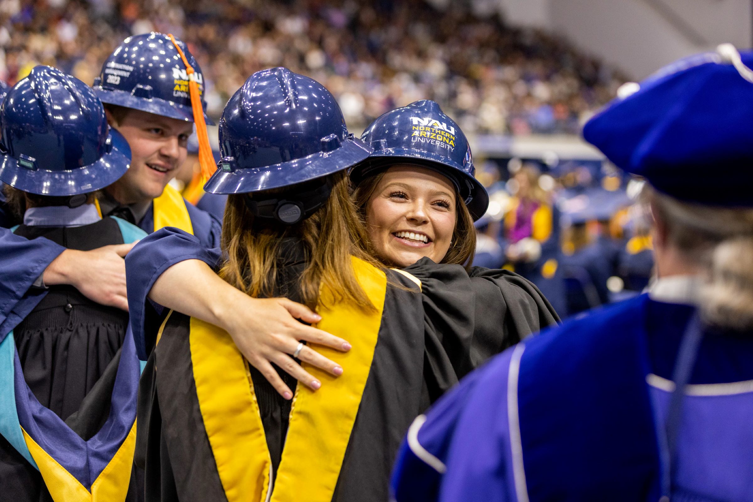 Students wearing construction hardhats embrace at N A U commencement.