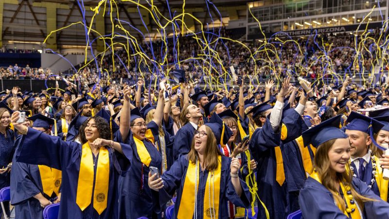 Confetti streamers fall from above as students celebrate graduation at N A U commencement.