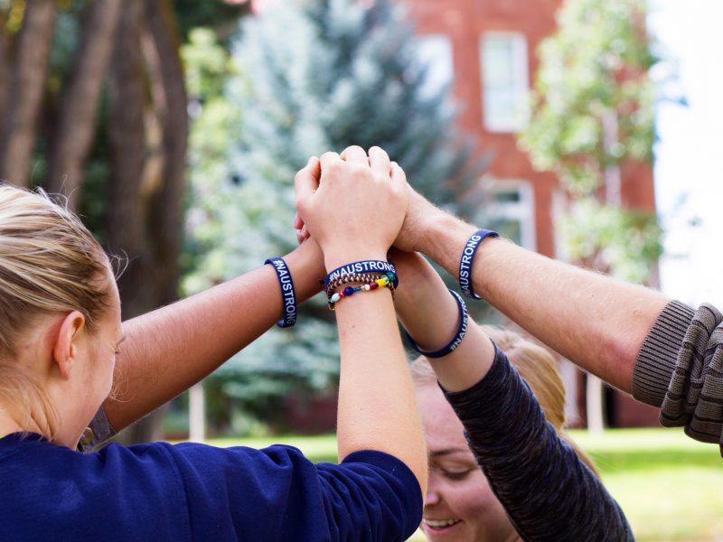 Students wearing N A U strong bracelets, stand in a circle putting their hands together in the middle.