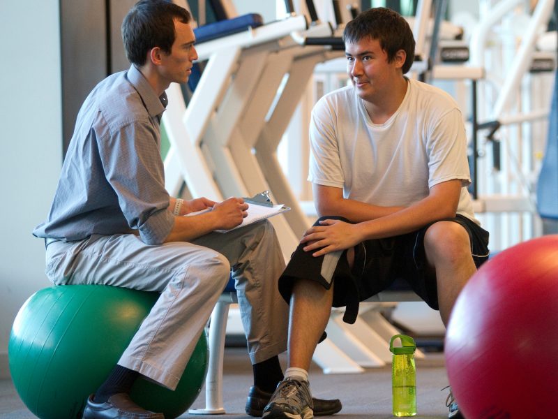 A physical therapist speaks with a patient wearing a knee brace.