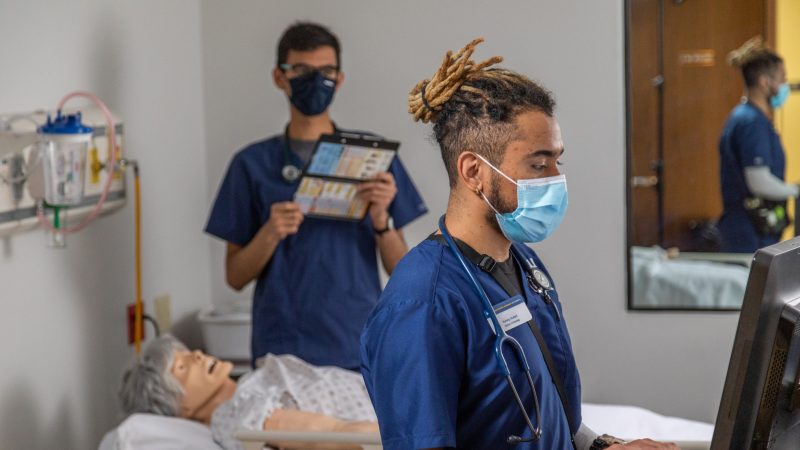 Nursing students in the College of Human and Health Services program read from a clipboard and add notes to a computer.