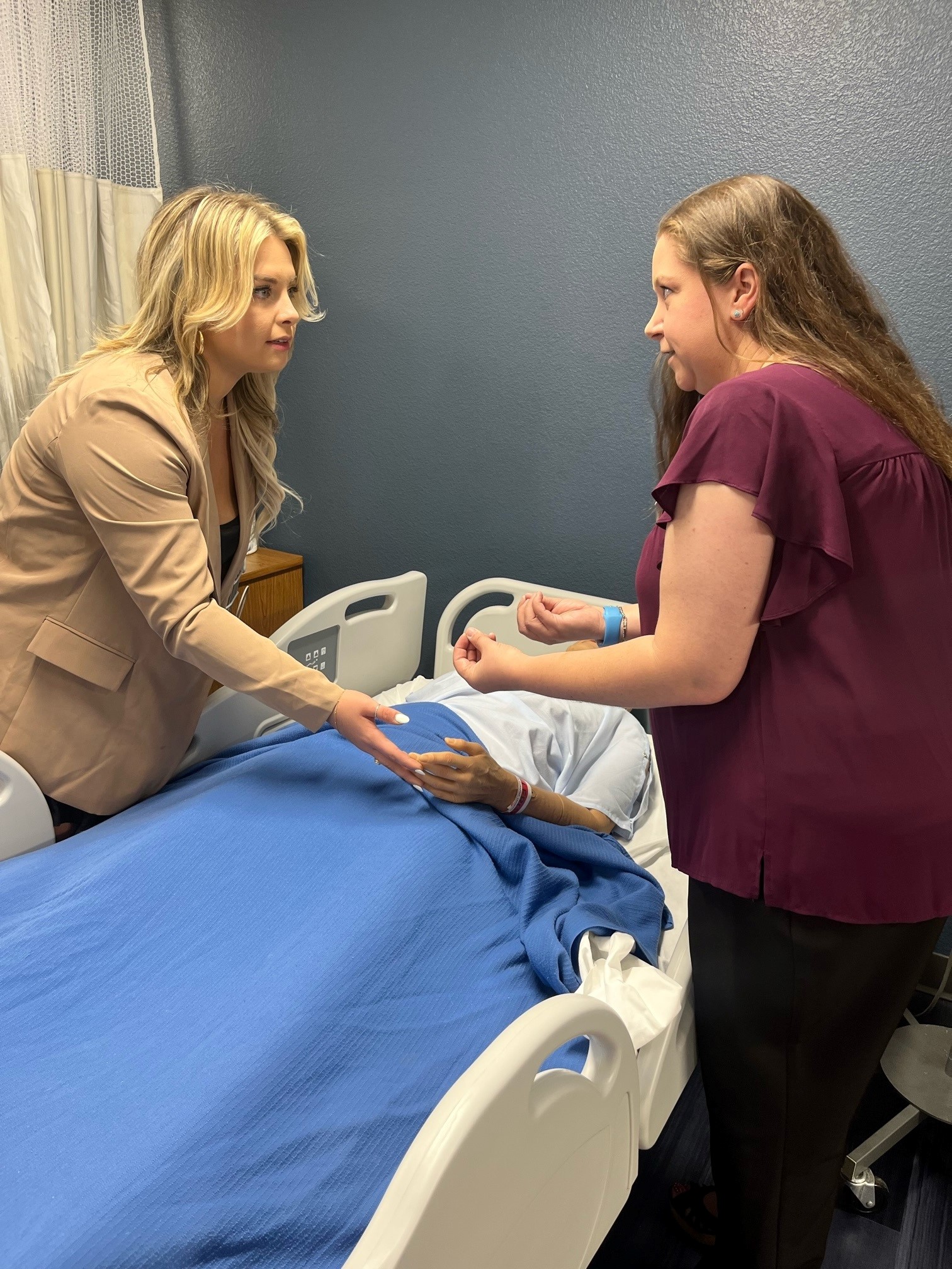 NAU nursing teacher demonstrates to a news anchor techniques using training doll.