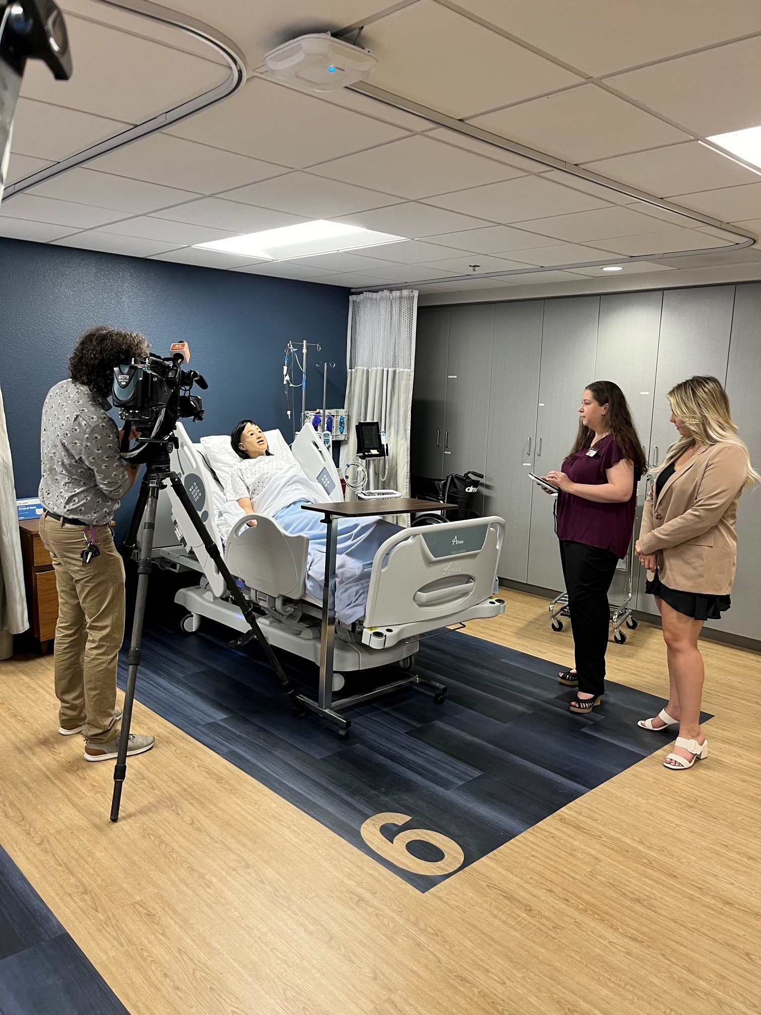 A news camera person focuses on the training doll during an interview about NAU's nursing program.
