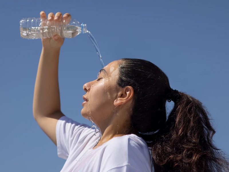 A woman in the sun pouring water on her head to cool down.