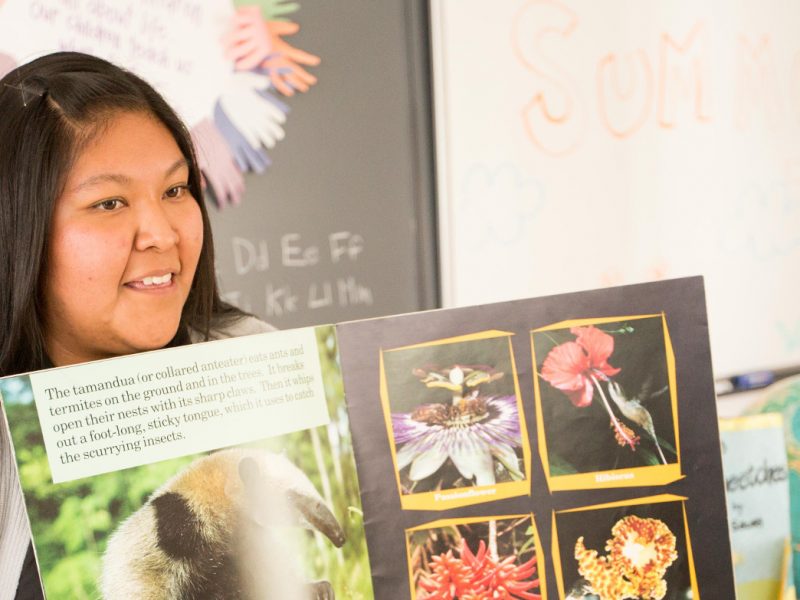 Student teacher sits in front of classroom and reads a book.