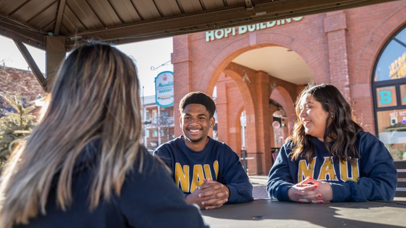 Three students sitting at a table outside talking to each other.