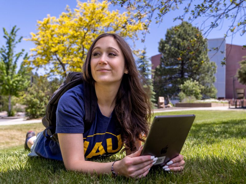 N A U student lying in the grass outside while working.