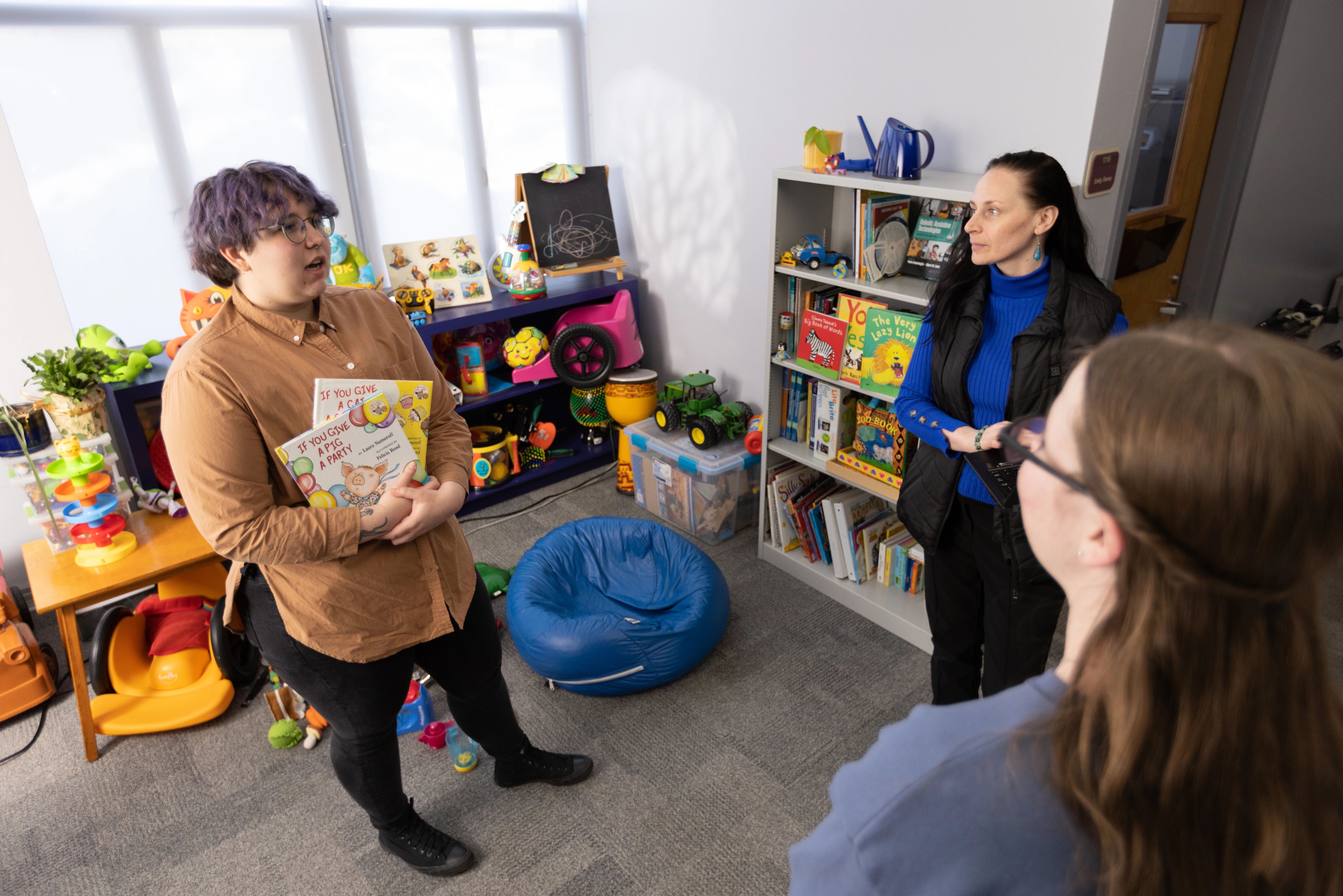 Three people standing in a classroom talking to each other.