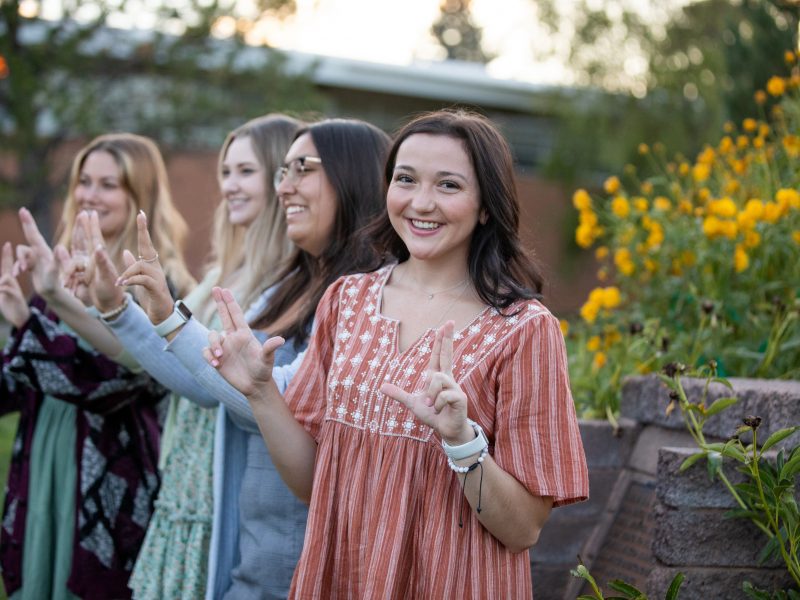 N A U students posing for camera outside, holding up both of their hands in the Lumberjack hand sign.