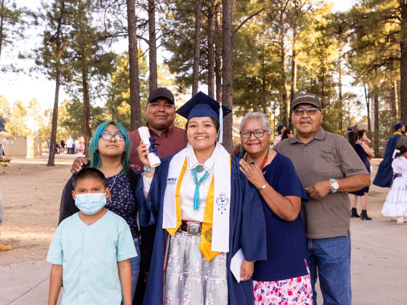 N A U student posing with her family in her cap and gown after commencement.