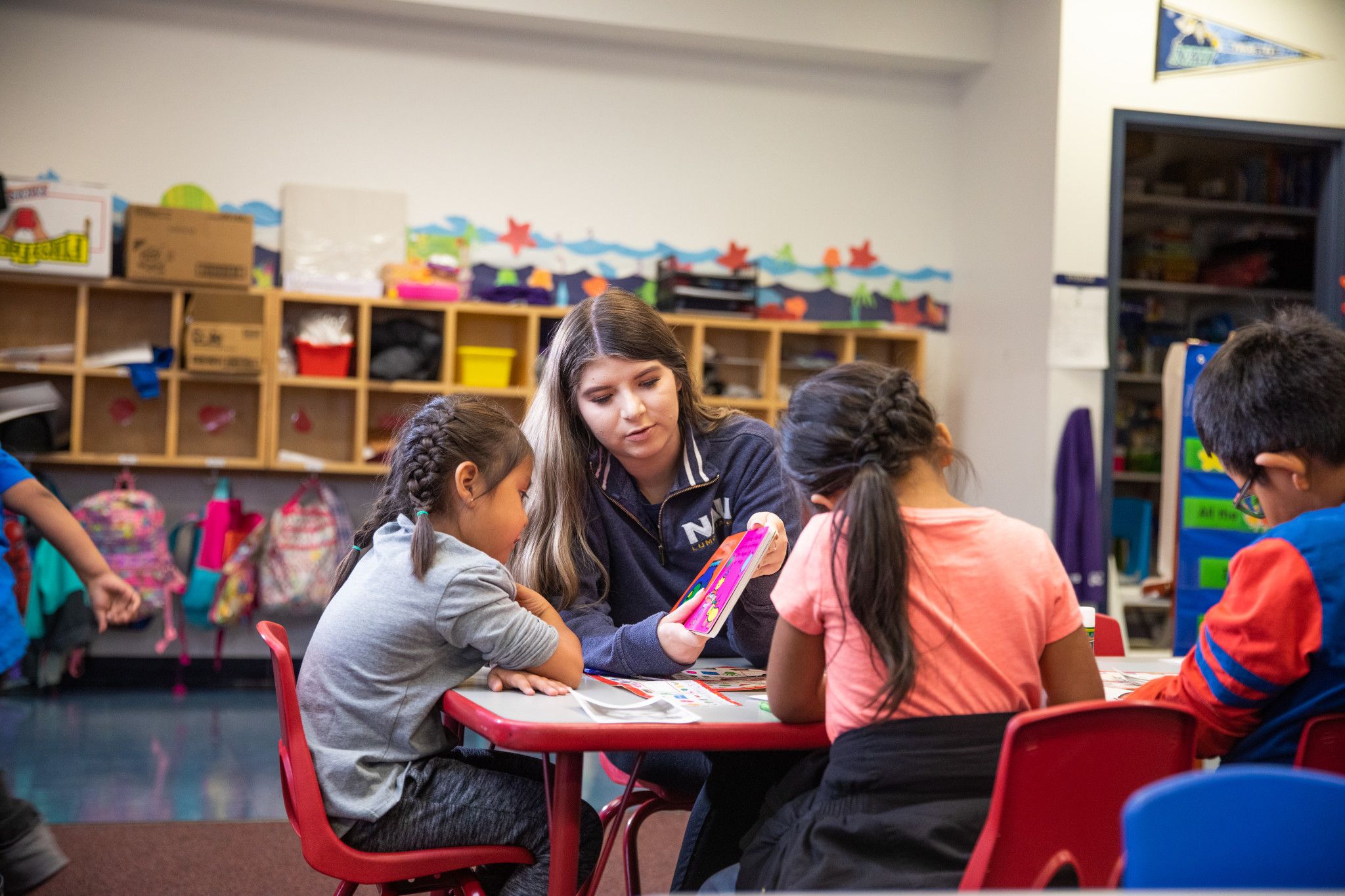 Student teacher helping elementary school kids with reading a book.