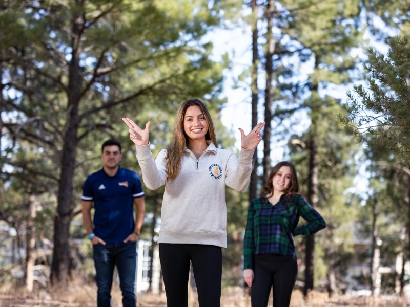 Student pose for a picture in the forest and using Jack's hand signal.