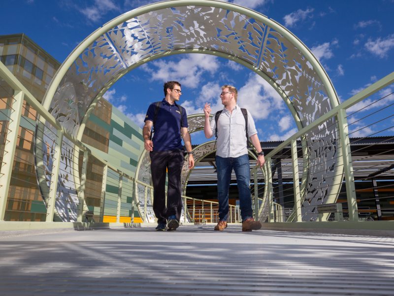 Two students walking outside underneath a decorative archway.