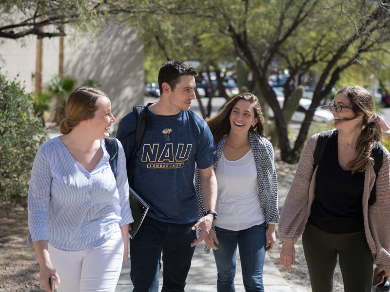 A group of four students walk on a sidewalk at Pima Community College.