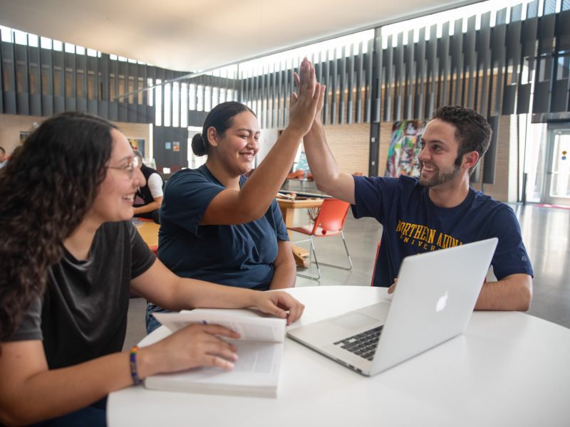Students working on a laptop and high fiving.