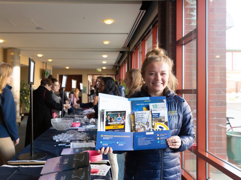 A photo of a student smiling while holding an N A U Orientation packet.