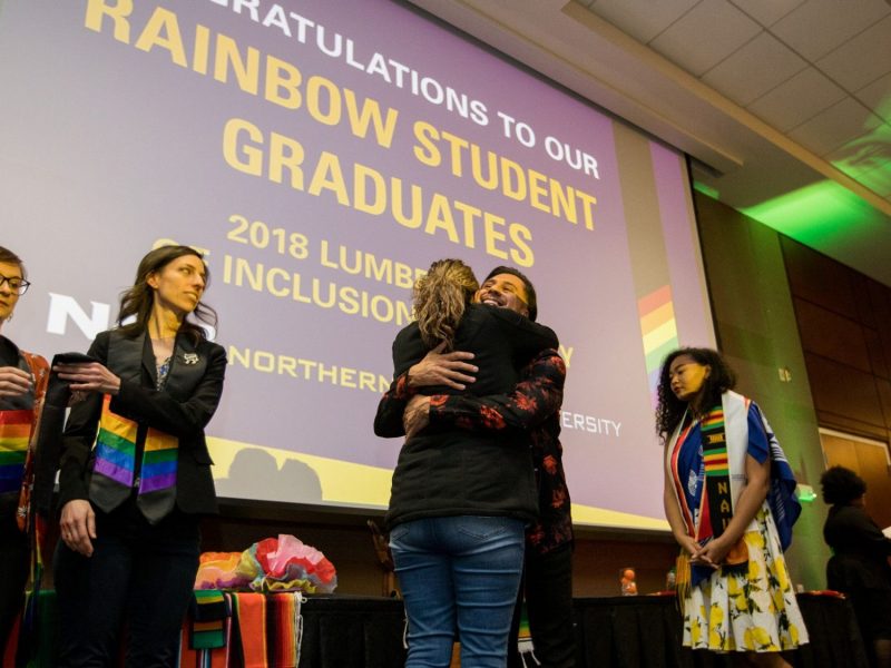 Students hug in front of a presentation screen that reads "Rainbow Student Graduates".